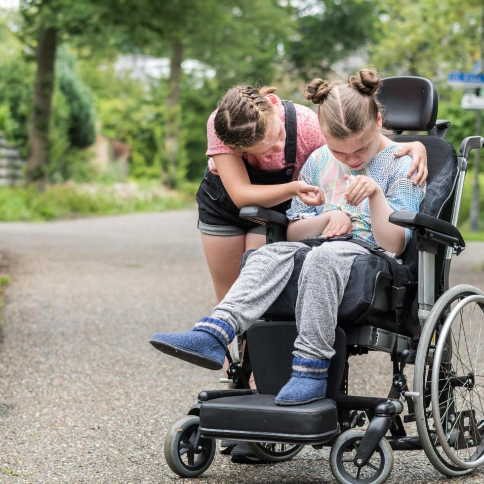 young girl helping another girl in a wheelchair